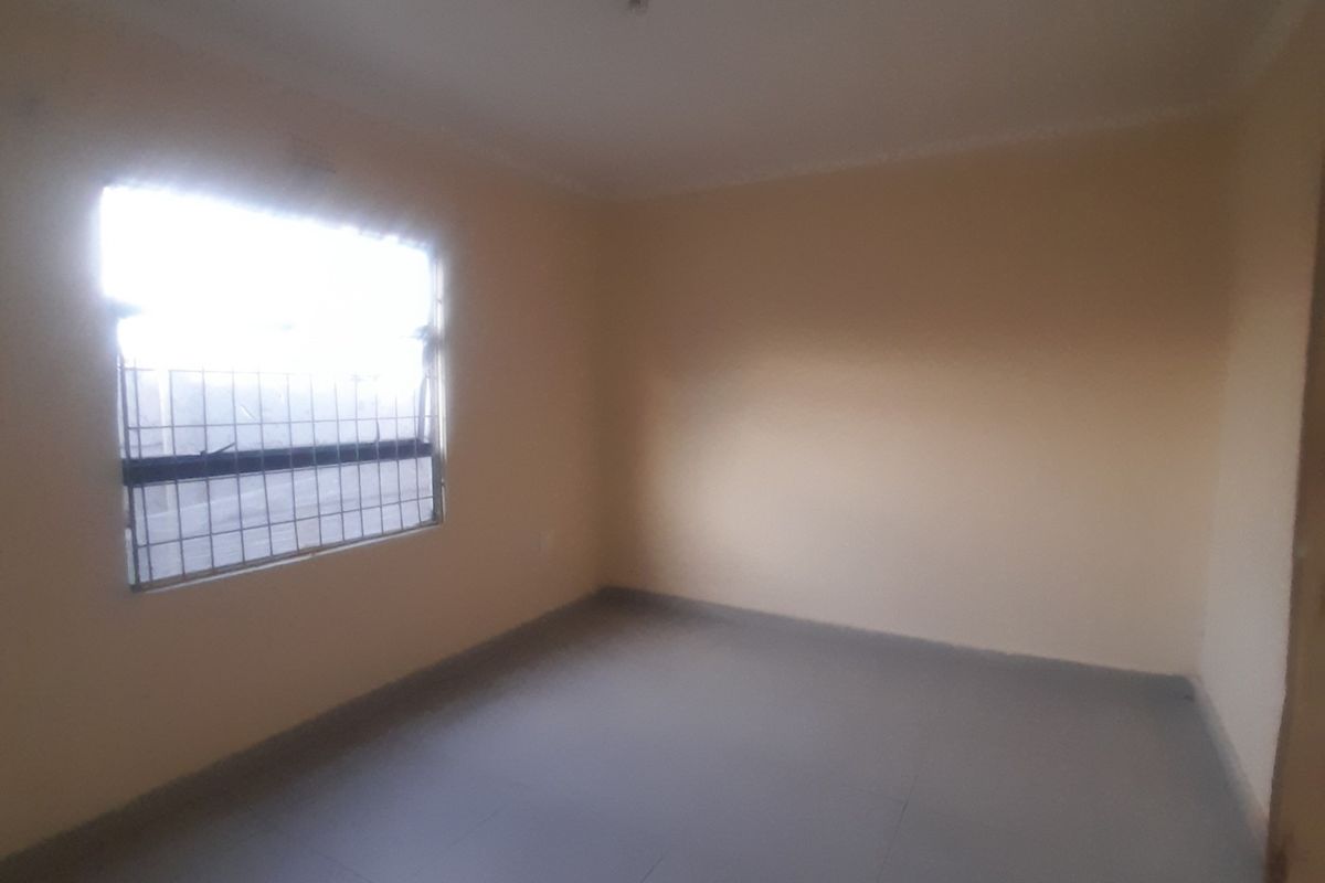 An empty bedroom featuring tiled flooring, neutral walls, and a window fitted with security bars.