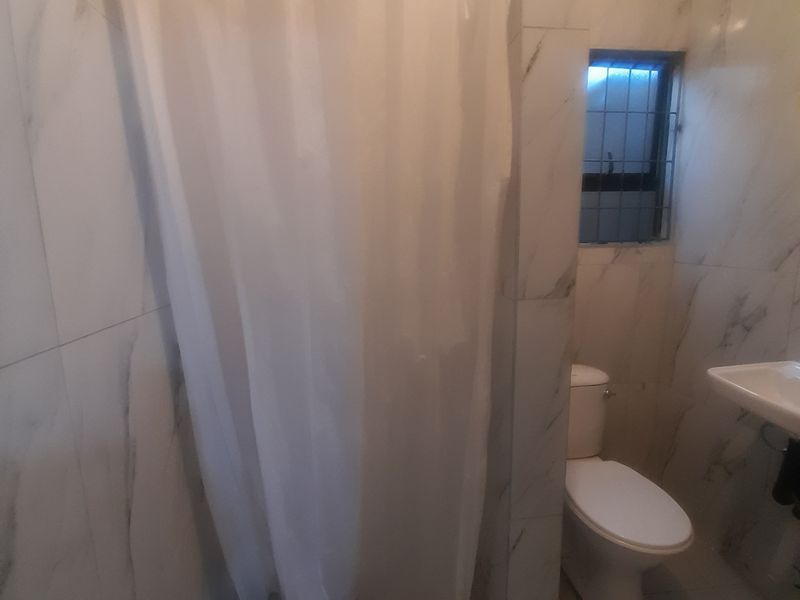 A functional bathroom featuring marble-look wall tiles, a shower with a curtain, a standard toilet, and a wall-mounted washbasin.