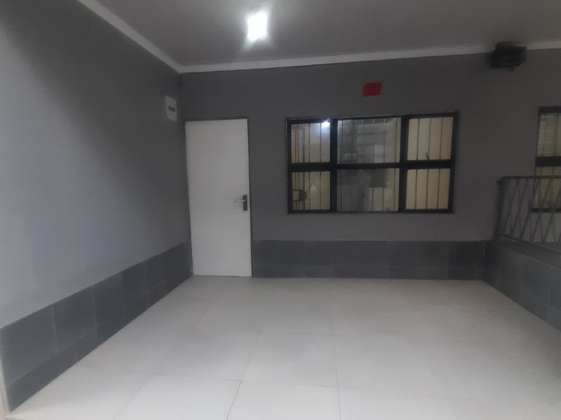 A clean, covered patio area featuring tiled flooring, security bars on the windows, and neutral grey wall finishes.