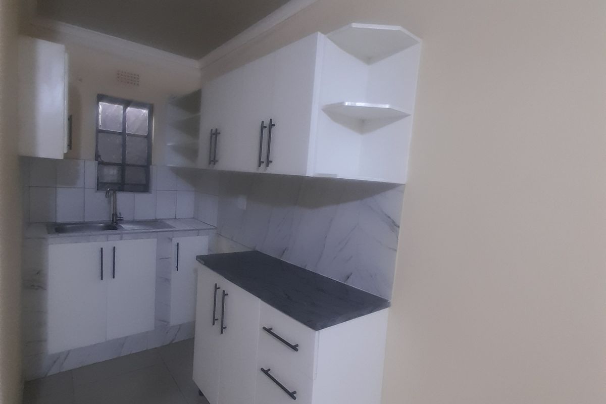 A clean, modern kitchen featuring white built-in cabinetry, dark countertops, tiled backsplash, and neutral floor tiles in a compact, functional layout.