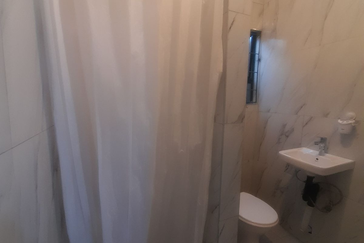 A compact bathroom featuring marble-effect wall tiles, a wall-mounted basin, a toilet, and a shower enclosure with a curtain.