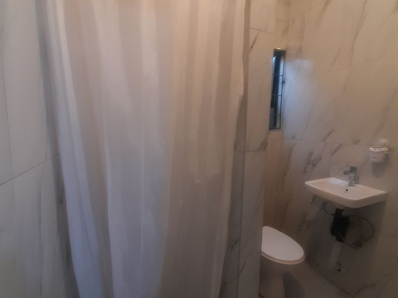 A compact bathroom featuring marble-effect wall tiles, a wall-mounted basin, a toilet, and a shower enclosure with a curtain.