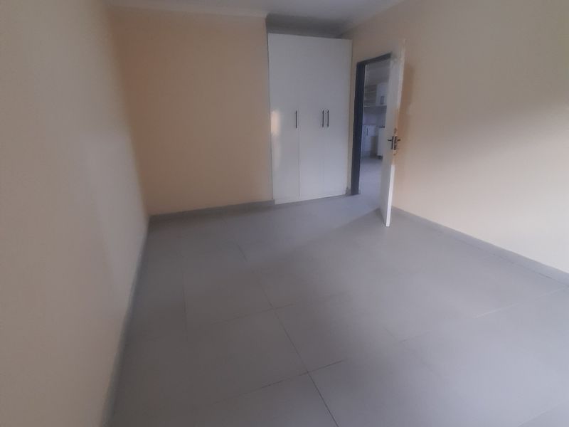 A clean, empty bedroom featuring neutral wall paint, grey tiled flooring, and a built-in white wardrobe.