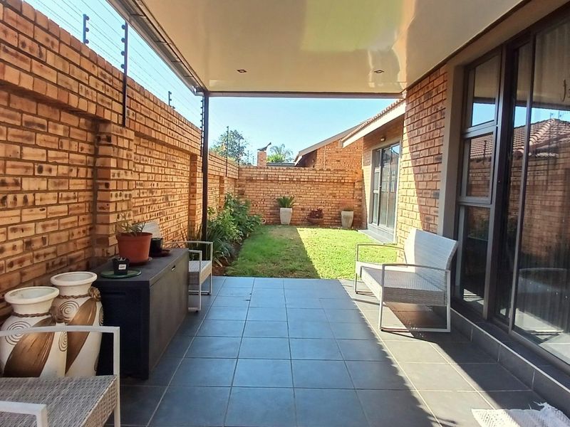 A covered patio featuring tiled flooring and facebrick walls, leading out to a private garden area with secure electric fencing.