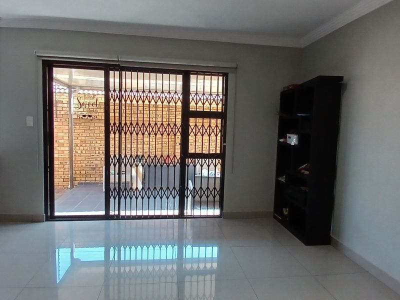 Open plan living area featuring tiled flooring, cove cornicing, and a sliding glass door with a security gate leading to the patio.