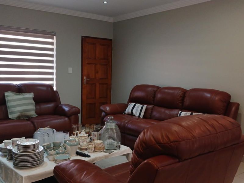 A comfortable living room featuring tiled flooring, recessed downlighting, and neutral wall tones, complemented by a wooden door and modern roller blinds.