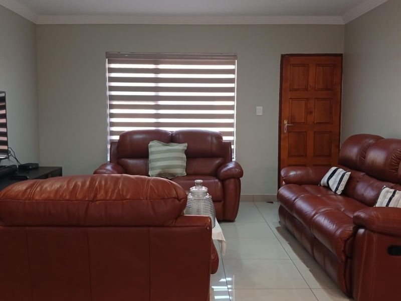 A well-maintained living room featuring neutral wall tones, tiled flooring, and a wooden door, providing a comfortable and functional space.