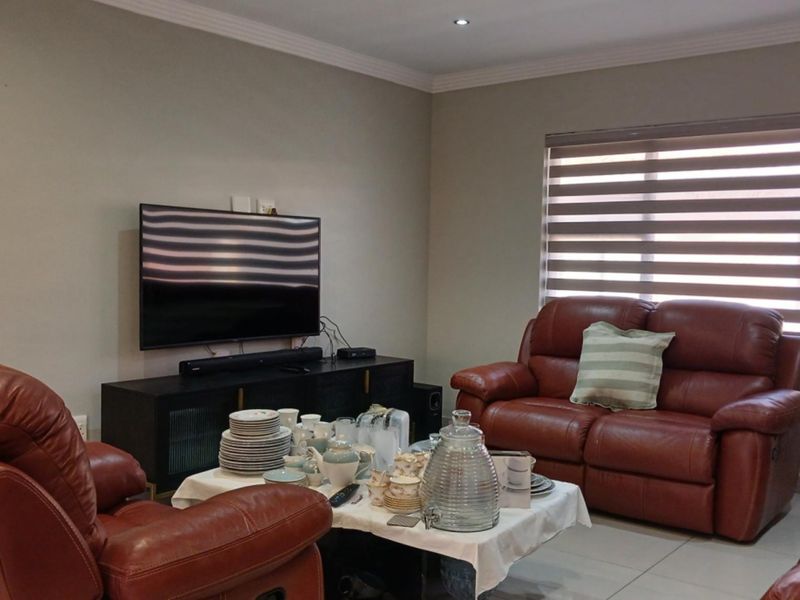 A comfortable living room featuring neutral wall tones, tiled flooring, recessed downlighting, and modern zebra blinds for adjustable natural light control.
