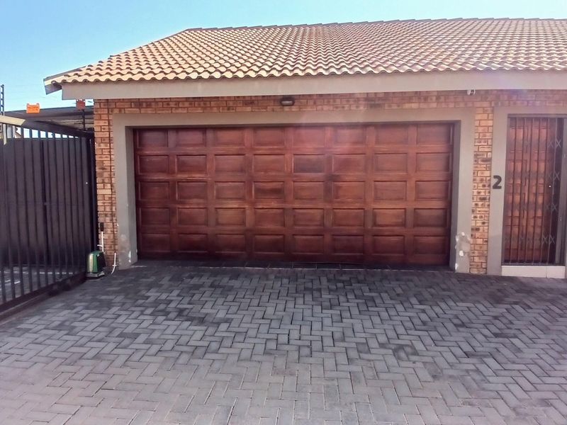 Front view of a cluster home featuring a paved driveway, a wooden garage door, and secure entrance with security gate.