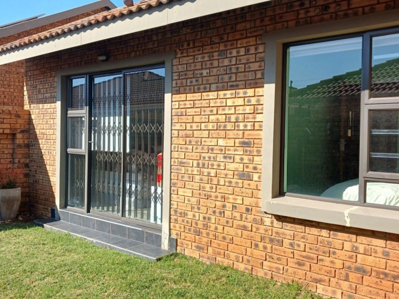 Rear exterior view of the cluster home featuring face brick walls, aluminium window frames, and a sliding glass door with security gate.