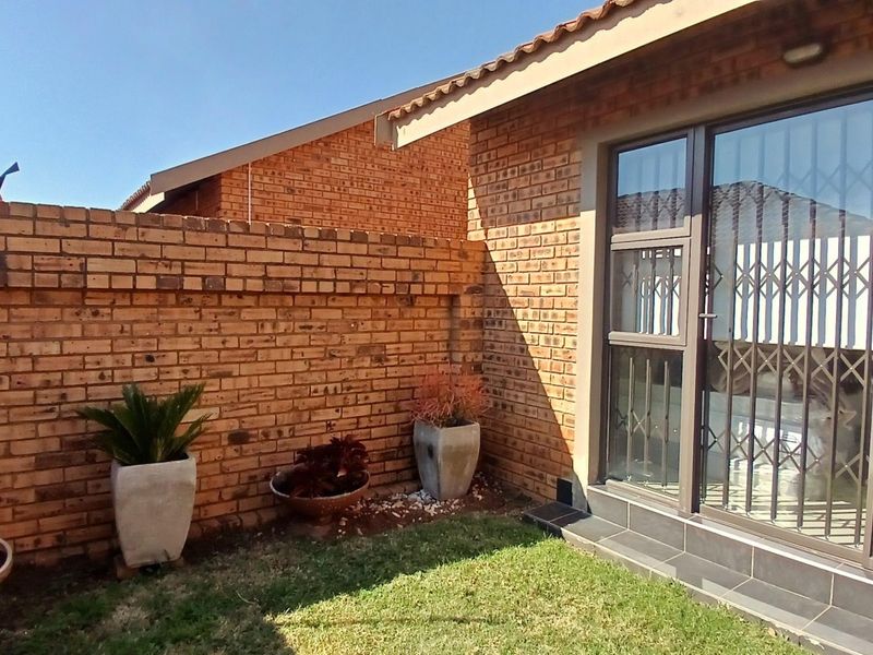 A private rear courtyard featuring face brick walls, a small lawn area, and a sliding glass door with a security gate.