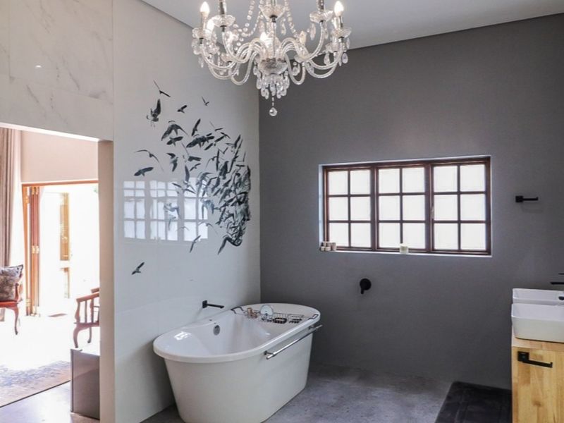 Modern bathroom featuring a freestanding bathtub, double vanity with wooden cabinetry, elegant chandelier lighting, and decorative wall tiling.