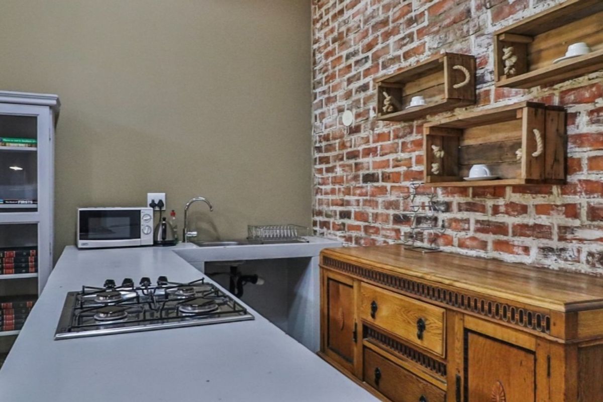 Kitchen area featuring an exposed brick wall, concrete countertop with integrated gas hob, and stainless steel sink.