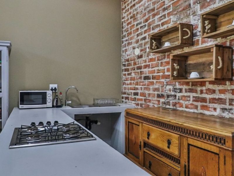 Kitchen area featuring an exposed brick wall, concrete countertop with integrated gas hob, and stainless steel sink.