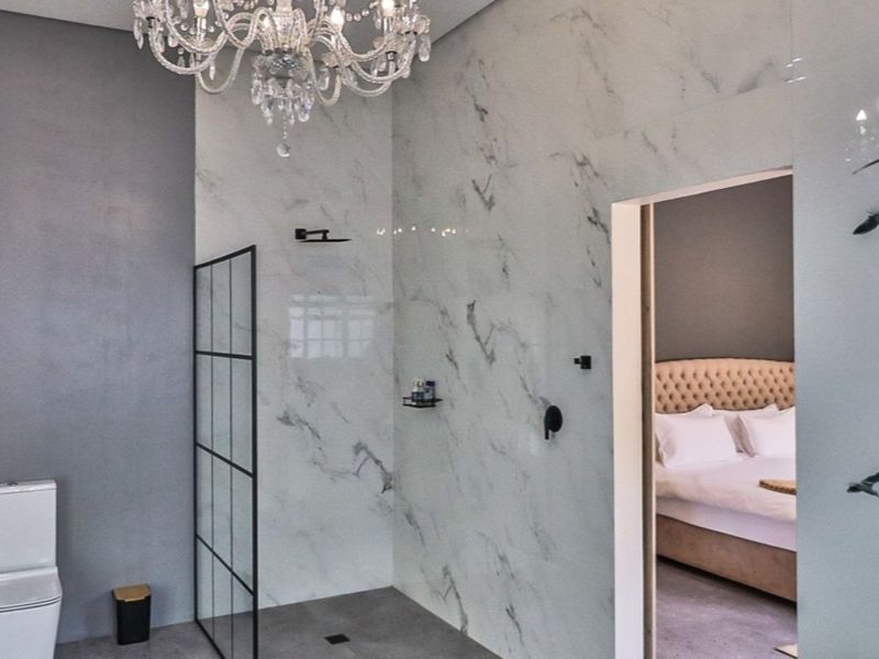 Modern bathroom featuring marble-look wall tiles, a walk-in shower with a black-framed screen, wall-mounted toilet, and an elegant crystal chandelier.