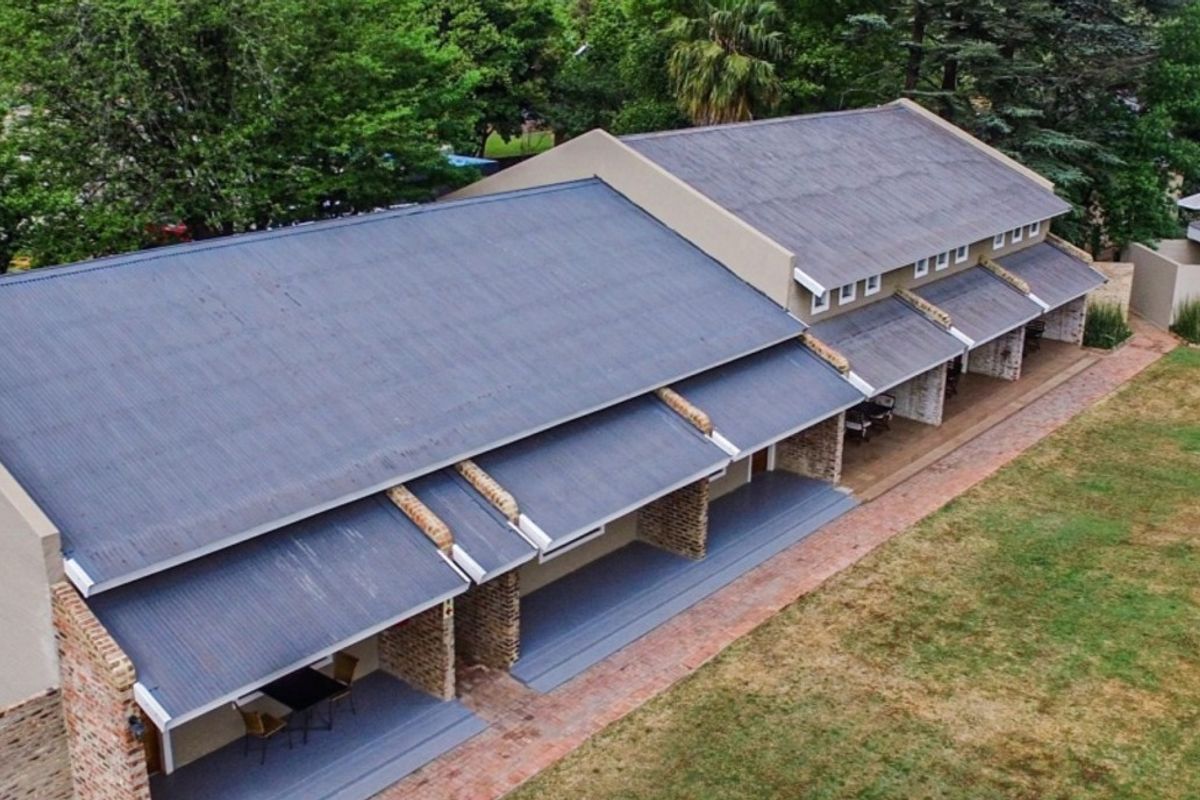 Aerial view of an apartment building featuring a corrugated metal roof, covered patio areas with brick pillars, and surrounding landscaped grounds.