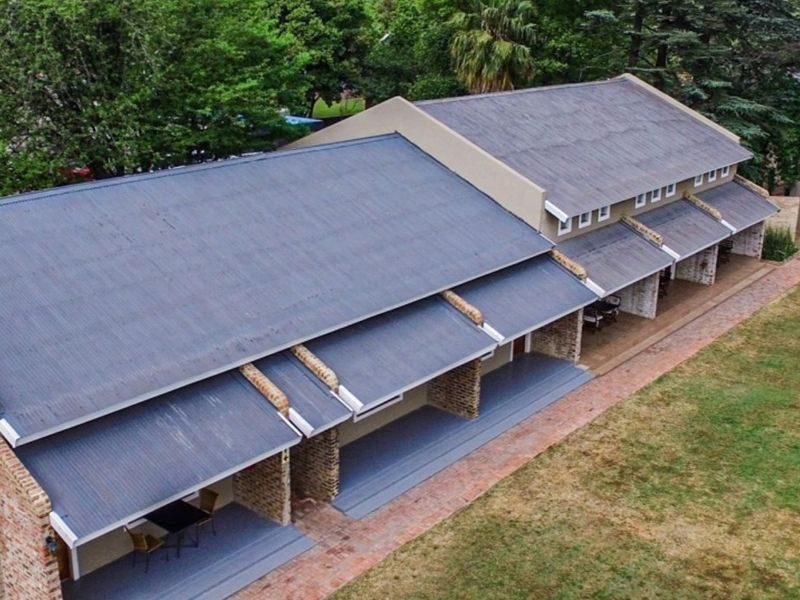 Aerial view of an apartment building featuring a corrugated metal roof, covered patio areas with brick pillars, and surrounding landscaped grounds.