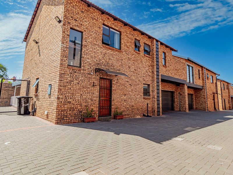 Front elevation of a face brick townhouse complex featuring paved driveway access, secure entrance, and integrated garage doors.