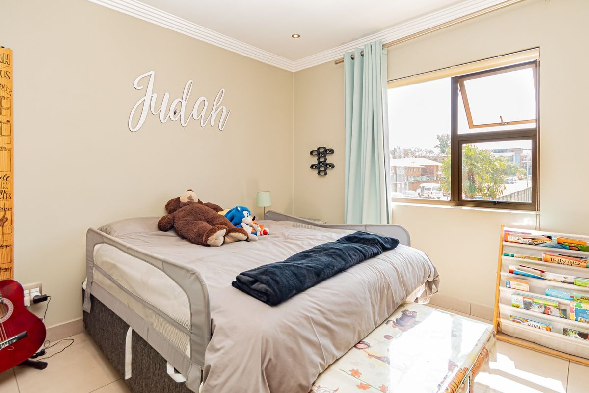 A well-maintained bedroom featuring tiled flooring, recessed downlighting, and a large aluminium-framed window providing natural light.