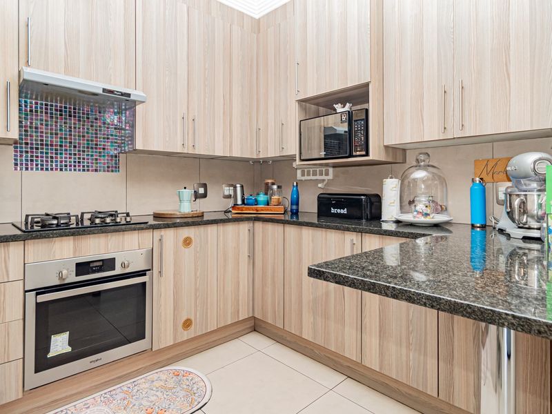 Modern kitchen featuring light wood-grain cabinetry, dark granite countertops, a gas hob, built-in oven, and a decorative mosaic tile splashback.