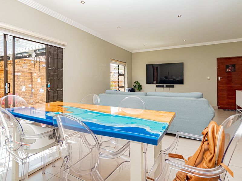 An open-plan living and dining area featuring tiled flooring, recessed downlights, and large sliding glass doors providing access to an outdoor patio space.