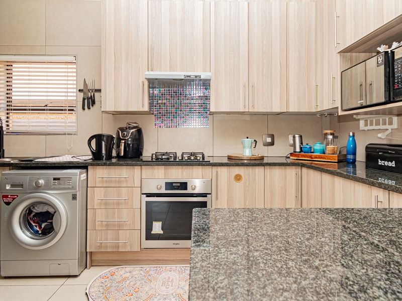 Modern kitchen featuring light wood-finish cabinetry, granite countertops, built-in oven, gas hob, and integrated laundry facilities.