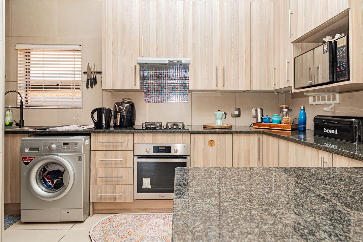Modern kitchen featuring light wood-finish cabinetry, granite countertops, built-in oven, gas hob, and integrated laundry facilities.