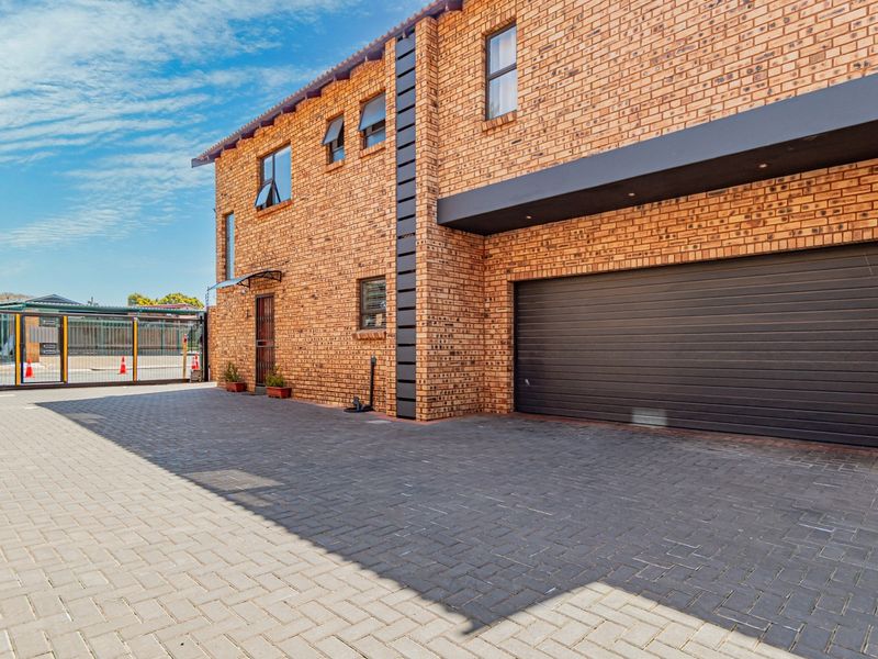 Front exterior view of a modern face brick townhouse featuring a paved driveway and an integrated automated garage.