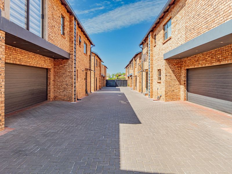 A view of the townhouse complex driveway featuring face brick facades, paved surfaces, and multiple automated garage doors.