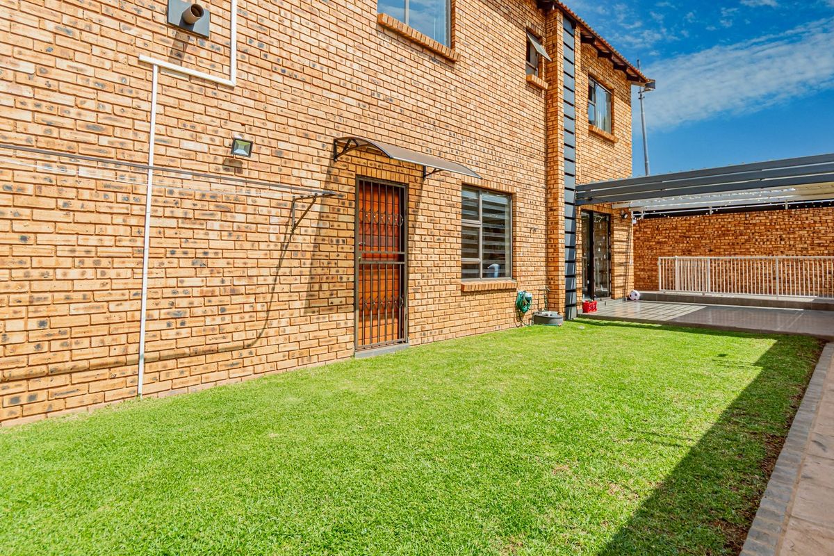 Rear view of the townhouse featuring a face brick facade, a small lawn, and a covered patio area.