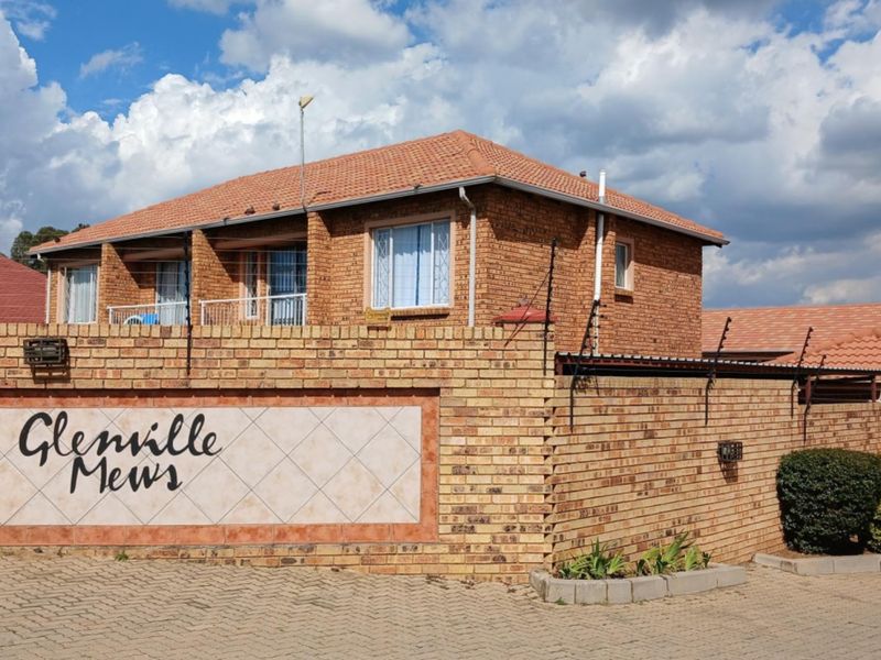 Front exterior view of a face brick townhouse complex featuring a tiled roof, perimeter wall with electric fencing, and paved driveway access.