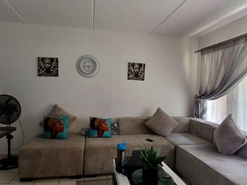 A living room area featuring tiled flooring and natural light through a window with curtain rails.