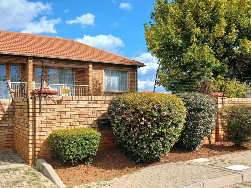 Front elevation of a face brick townhouse featuring a tiled roof, paved driveway, and secure boundary wall with electric fencing.