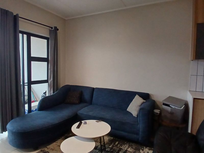 Open plan living area featuring tiled flooring and a sliding glass door leading to a balcony, adjacent to a compact kitchen space.