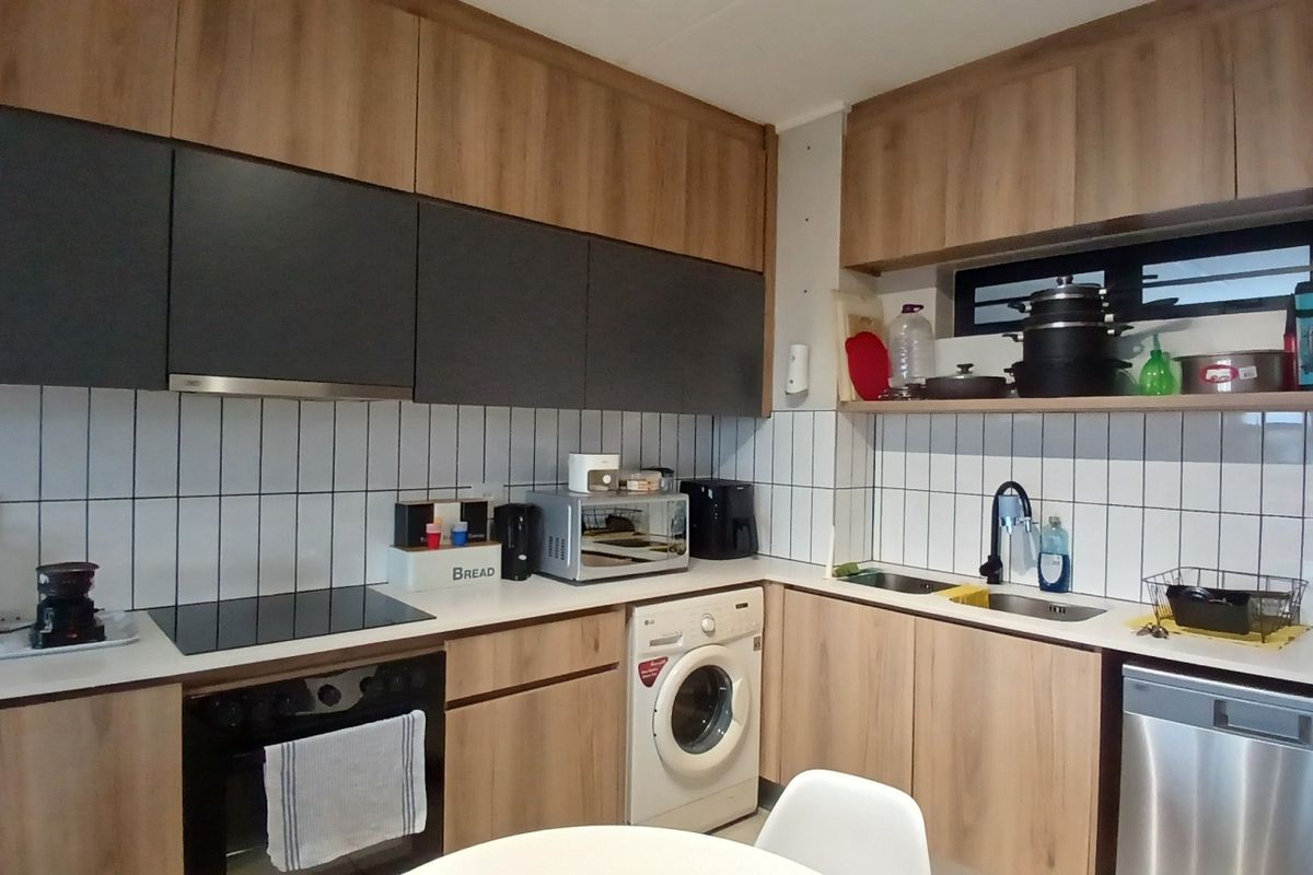 Modern kitchen featuring wood-tone and dark grey cabinetry, tiled backsplash, integrated appliances including a washing machine, dishwasher, and built-in oven with hob.