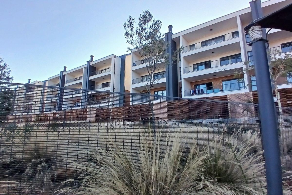 Exterior view of a modern apartment complex featuring multiple levels with private balconies, brick detailing, and secure perimeter fencing.