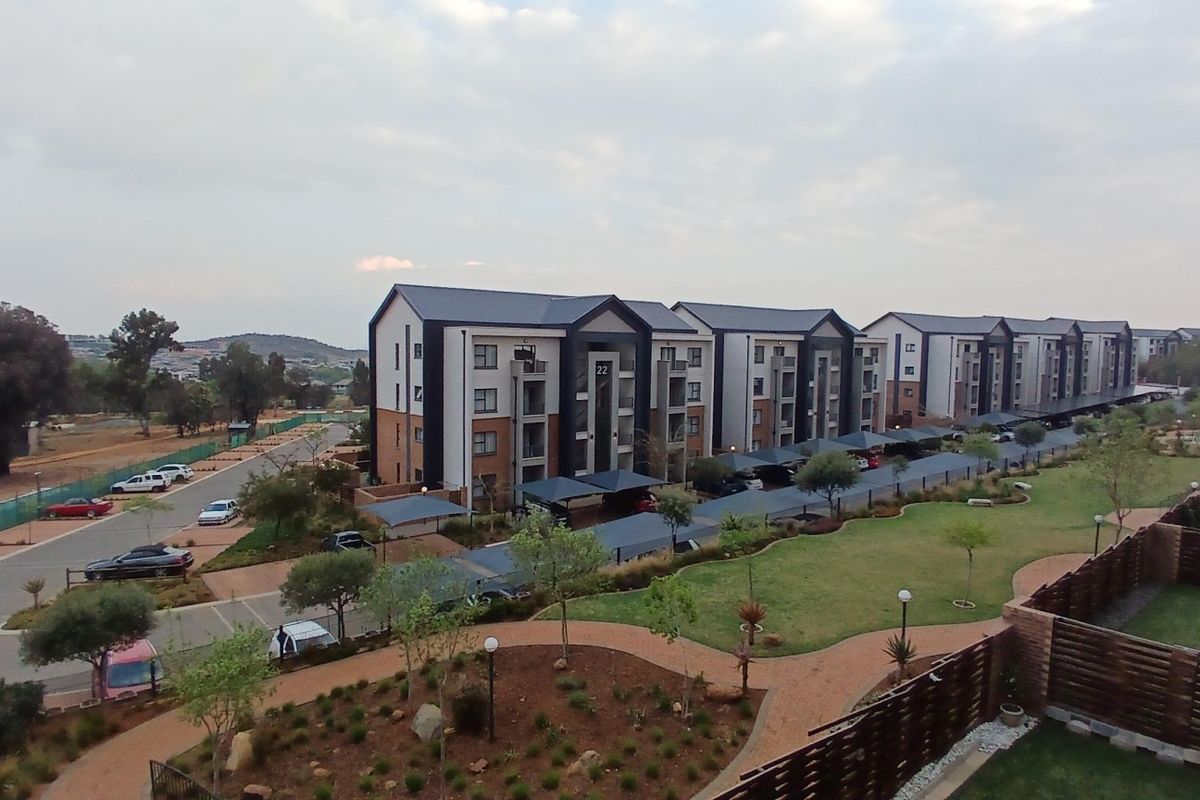 An elevated aerial view of a modern apartment complex featuring multi-story residential blocks, covered parking facilities, and well-maintained communal landscaped gardens.