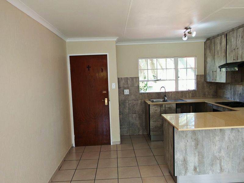 A functional kitchen featuring built-in cabinetry, laminate countertops, a hob with extractor fan, and tiled flooring in an open-plan layout.