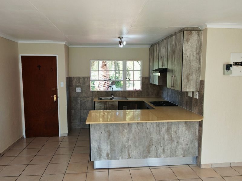 A functional kitchen featuring built-in cabinetry, laminate countertops, a hob with extractor fan, and tiled flooring in an open-plan layout.