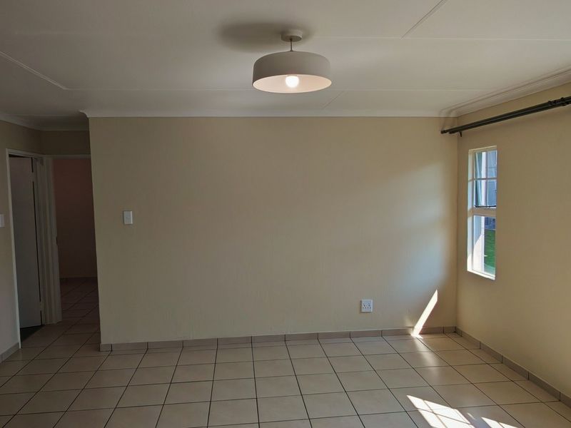An open-plan living area featuring neutral wall tones, tiled flooring, and a functional kitchen corner, offering a bright and versatile space for living and dining.