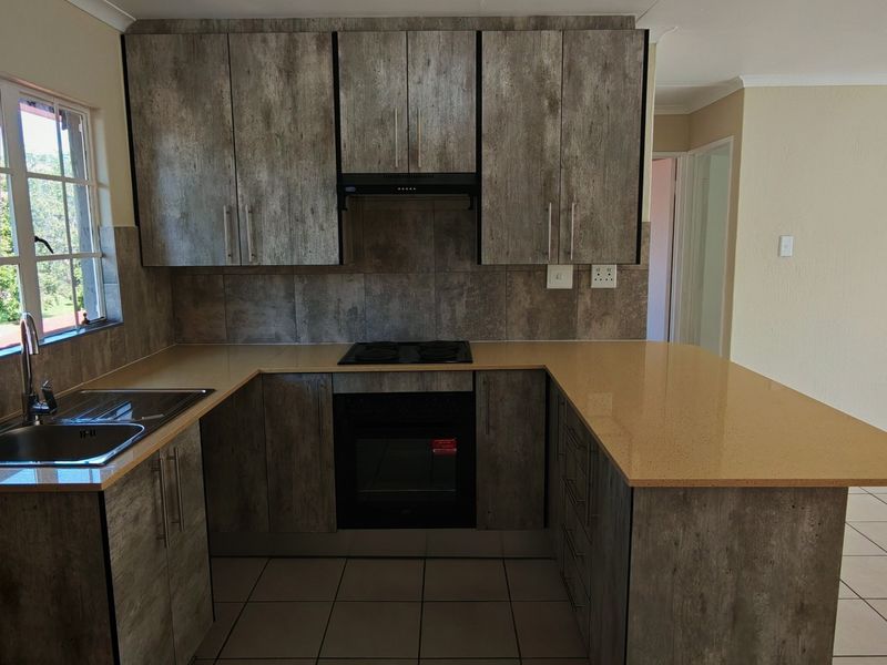 Modern kitchen featuring stone countertops, built-in oven, hob, extractor fan, and ample cabinetry, with tiled flooring and a view of the garden.