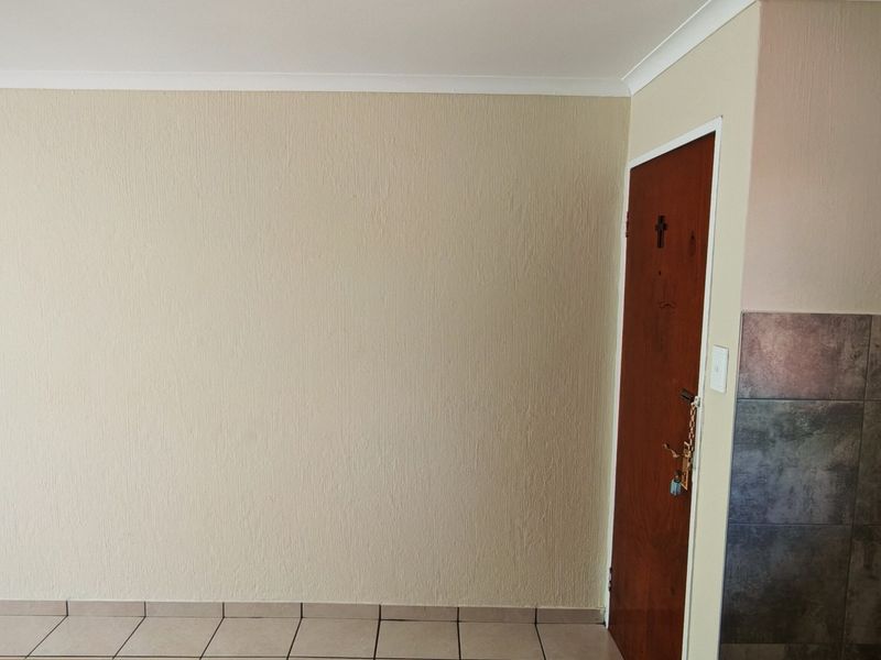 An empty living area featuring neutral textured walls, tiled flooring, and a tiled accent wall section near the doorway.