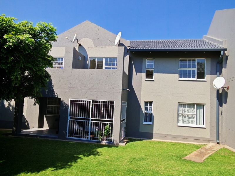 Rear view of a townhouse featuring a grey rendered facade, tiled roof, and a small private garden area.