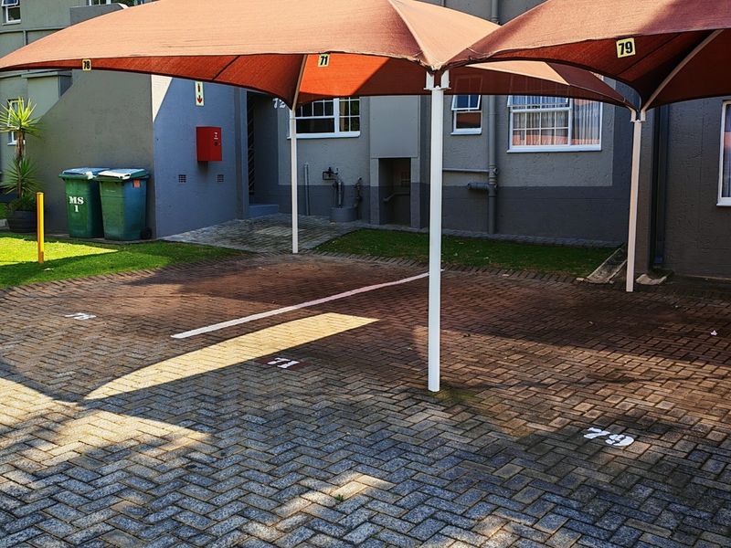Exterior view of a townhouse complex featuring paved parking bays with shade cloth carports and numbered designated spaces.