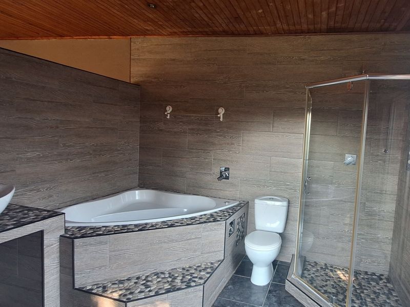 A modern bathroom featuring a corner bathtub, glass shower enclosure, vessel sink, and wood-look wall tiling with pebble accents and a timber ceiling.