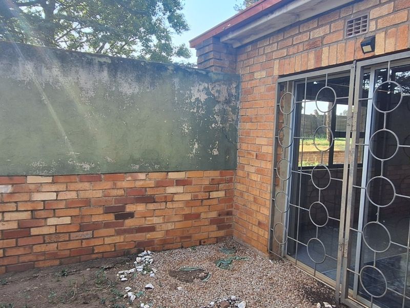 Rear exterior view showing a face brick wall, sliding door with security gate, and a weathered boundary wall requiring maintenance.