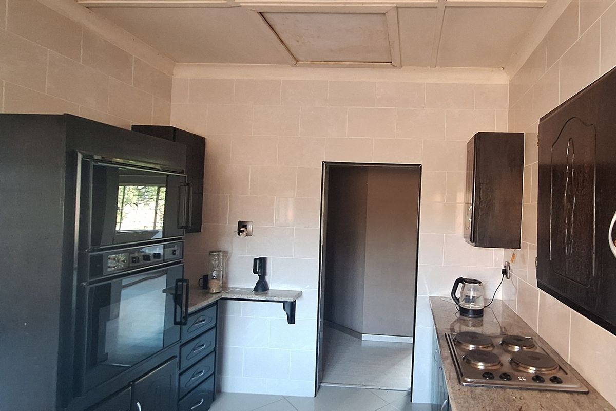 A functional kitchen featuring dark built-in cabinetry, granite countertops, an integrated oven, and an electric hob with tiled wall finishes.