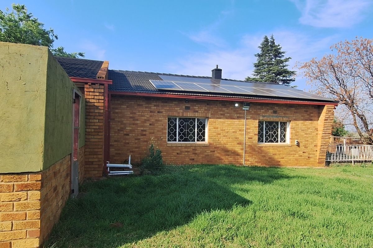 Rear view of a brick-built small holding featuring a tiled roof, installed solar panels, and security bars on the windows.