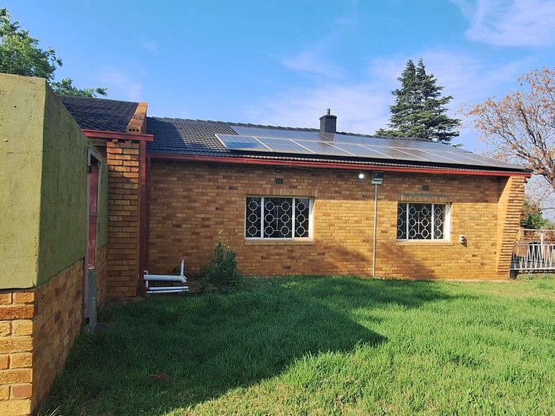 Rear view of a brick-built small holding featuring a tiled roof, installed solar panels, and security bars on the windows.
