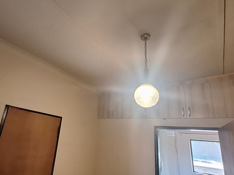 A bedroom interior featuring built-in wooden cupboards and a central pendant light fixture.